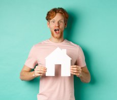 Formation Chargé(e) de copropriété en Haute Savoie concept-immobilier-rousse-excite-barbe-montrant-decoupe-maison-papier-souffle-coupe-regardant-fascine-par-camera-debout-fond-menthe